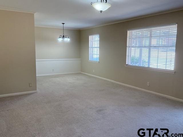 carpeted empty room with a chandelier, crown molding, and baseboards