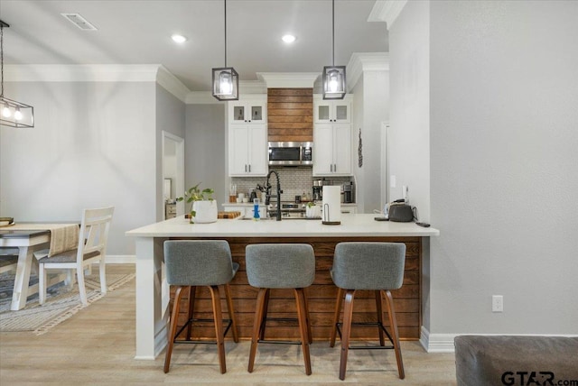 bar featuring tasteful backsplash, light hardwood / wood-style flooring, ornamental molding, pendant lighting, and white cabinets