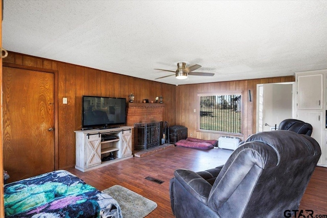 living room featuring dark hardwood / wood-style flooring, wooden walls, a textured ceiling, and ceiling fan