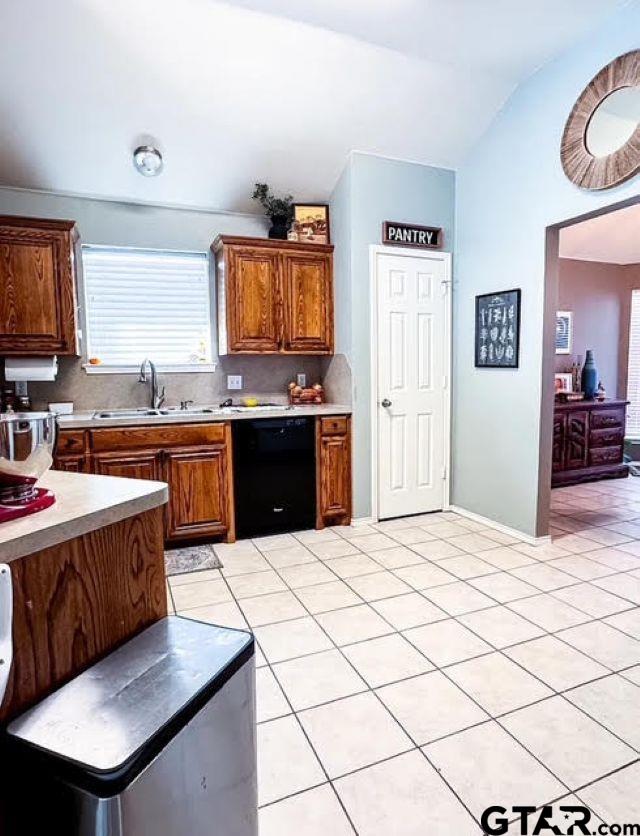 kitchen with dishwasher, sink, vaulted ceiling, light tile patterned floors, and tasteful backsplash