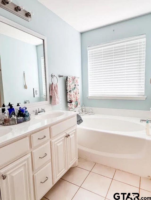 bathroom with a wealth of natural light, a sink, tile patterned flooring, double vanity, and a bath