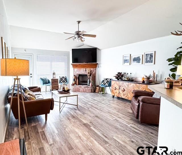 living area with ceiling fan, wood finished floors, a fireplace, and vaulted ceiling