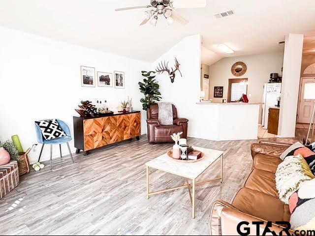 living room featuring light wood-type flooring, visible vents, ceiling fan, and vaulted ceiling