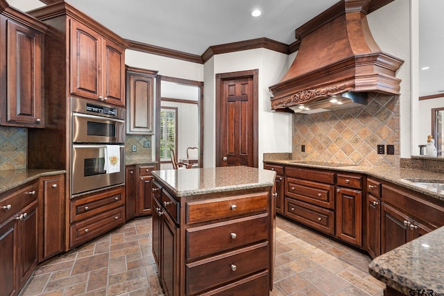 kitchen featuring a kitchen island, double oven, light stone counters, custom range hood, and black electric cooktop