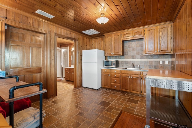 kitchen with sink, wood ceiling, wooden walls, white fridge, and backsplash