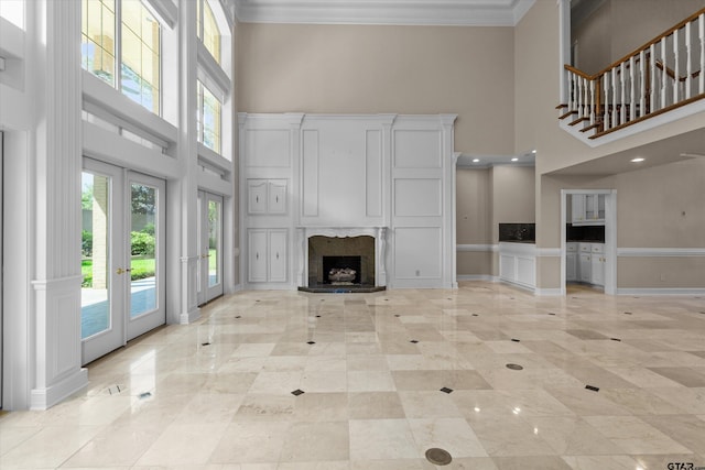 unfurnished living room featuring crown molding, a towering ceiling, a fireplace, and french doors