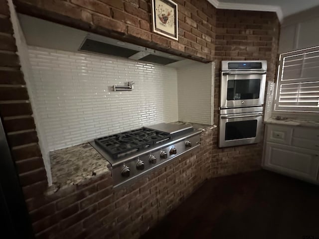 kitchen with brick wall, light stone countertops, crown molding, and stainless steel appliances