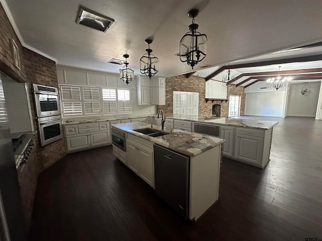 kitchen featuring lofted ceiling, a wealth of natural light, decorative light fixtures, and an island with sink