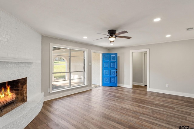 unfurnished living room with crown molding, a brick fireplace, hardwood / wood-style flooring, and ceiling fan