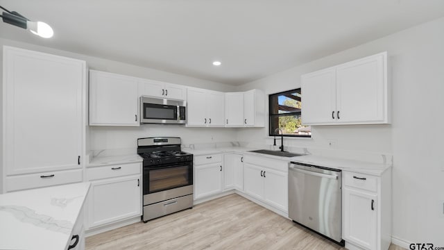 kitchen featuring sink, light stone counters, light hardwood / wood-style floors, white cabinets, and appliances with stainless steel finishes