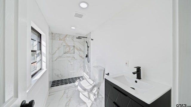 bathroom with a tile shower, vanity, and toilet