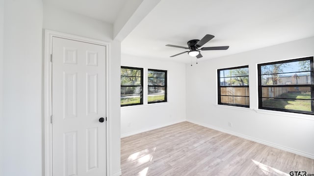 empty room featuring plenty of natural light, ceiling fan, and light wood-type flooring