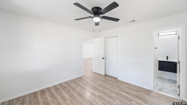 unfurnished bedroom with light wood-type flooring, a closet, ensuite bath, and ceiling fan