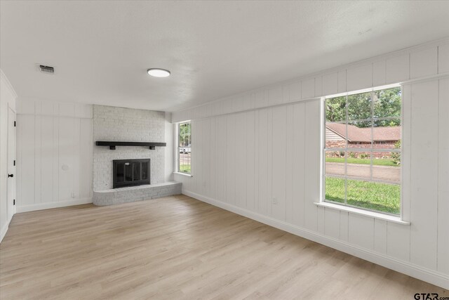 2002 Friendly Ave, Mount Pleasant, TX 75455 - unfurnished living room with light wood-type flooring, a decorative wall, baseboards, plenty of natural light, and a brick fireplace