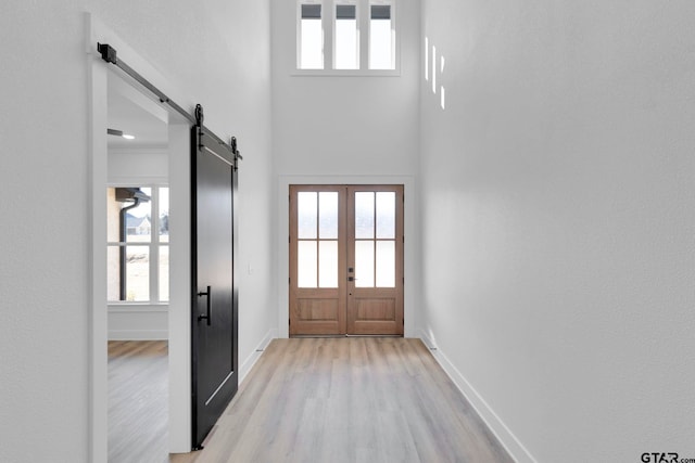 doorway to outside featuring light wood-type flooring, a barn door, and a high ceiling