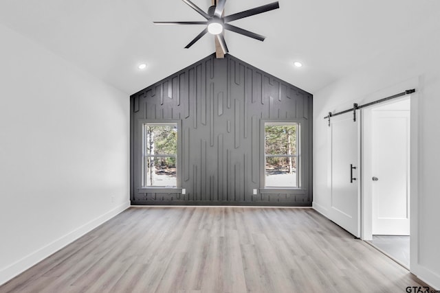 spare room with light wood-type flooring, a barn door, vaulted ceiling, and ceiling fan