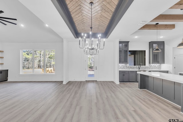 kitchen featuring gray cabinets, a raised ceiling, tasteful backsplash, hanging light fixtures, and light hardwood / wood-style flooring