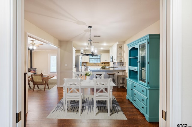dining area with a wood stove, an inviting chandelier, and dark hardwood / wood-style floors