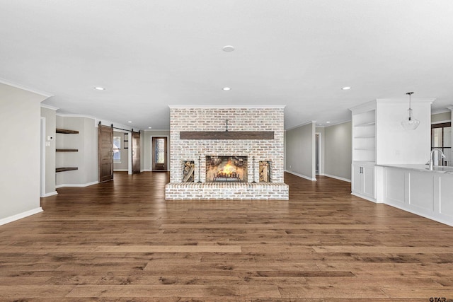 unfurnished living room with dark wood-type flooring, a barn door, ornamental molding, and a brick fireplace