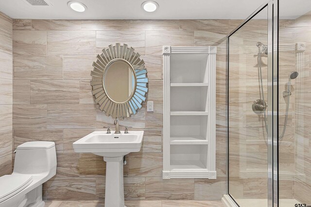 bathroom featuring toilet, tile walls, and a shower with shower door