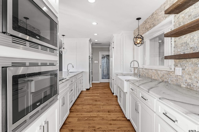 kitchen featuring hardwood / wood-style flooring, white cabinetry, sink, hanging light fixtures, and stainless steel microwave