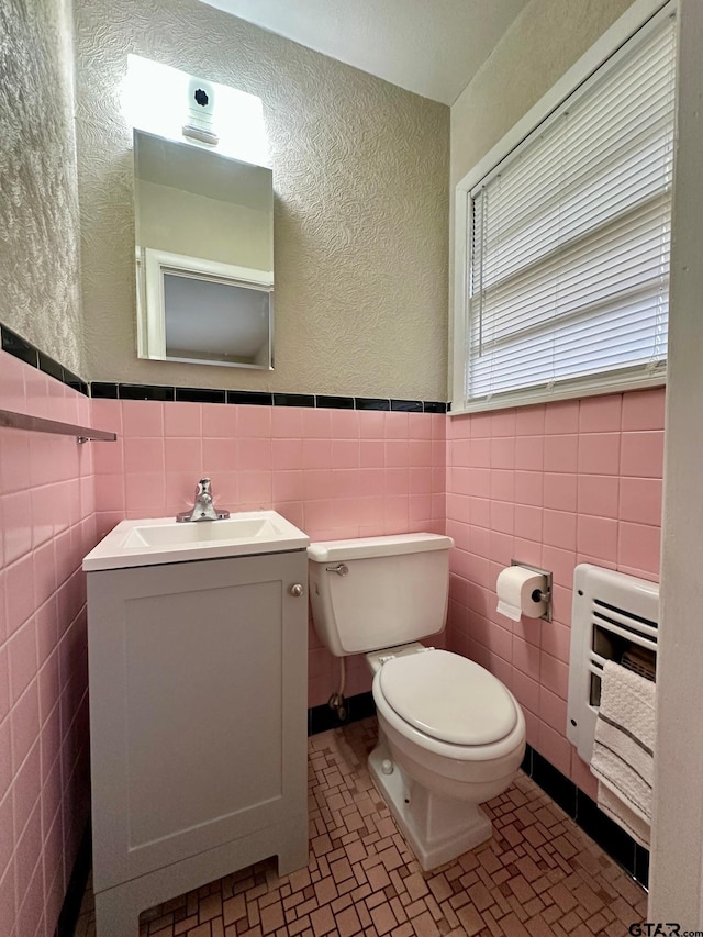 half bathroom with tile walls, toilet, vanity, a textured wall, and wainscoting