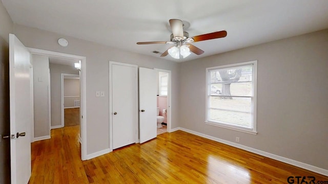 unfurnished bedroom featuring light wood-style flooring, ensuite bath, baseboards, visible vents, and ceiling fan