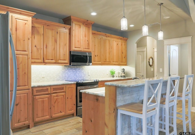 kitchen featuring light stone counters, backsplash, decorative light fixtures, a center island with sink, and appliances with stainless steel finishes