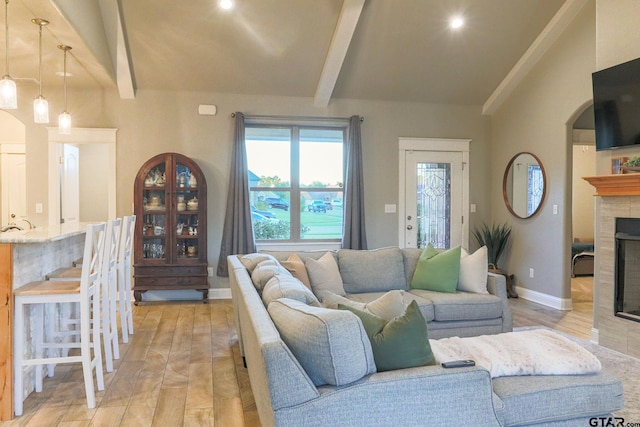 living room featuring lofted ceiling with beams, light hardwood / wood-style floors, and a tile fireplace