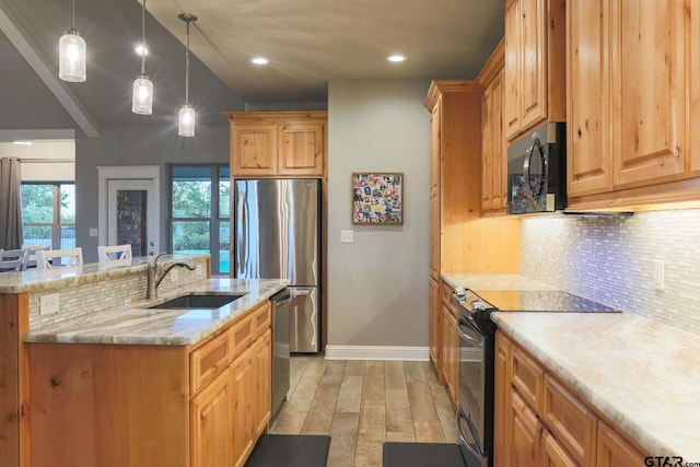 kitchen with sink, hanging light fixtures, light hardwood / wood-style floors, a kitchen bar, and black appliances