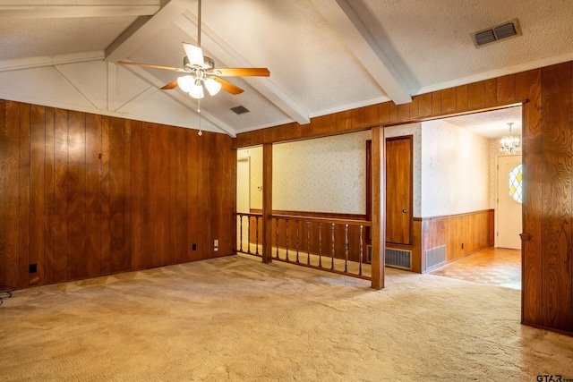 carpeted empty room featuring lofted ceiling with beams, visible vents, wooden walls, and a textured ceiling