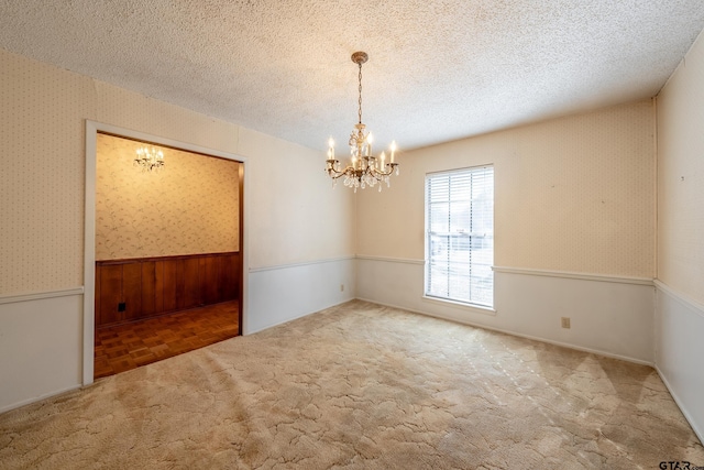 empty room with a wainscoted wall, a textured ceiling, a chandelier, and wallpapered walls