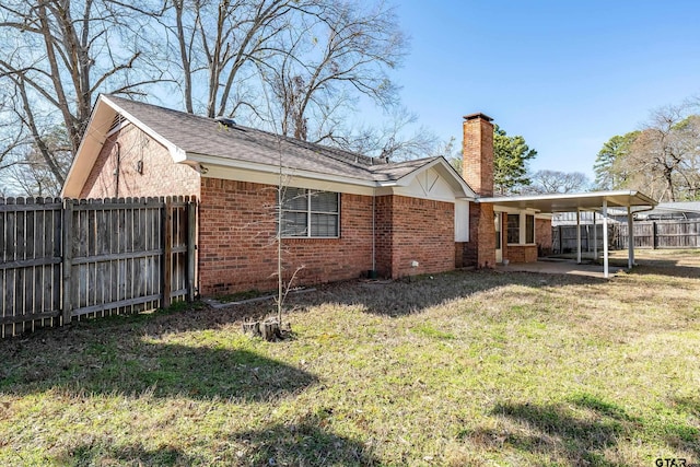 back of property featuring a chimney, an attached carport, fence, a yard, and brick siding