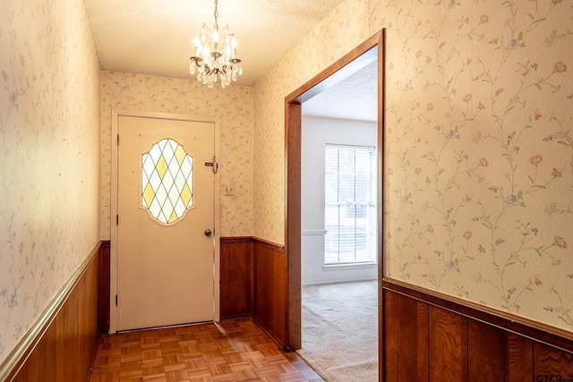 entryway with wallpapered walls, a textured ceiling, a wainscoted wall, and an inviting chandelier