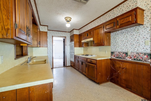 kitchen with a textured ceiling, white appliances, a sink, light countertops, and wallpapered walls