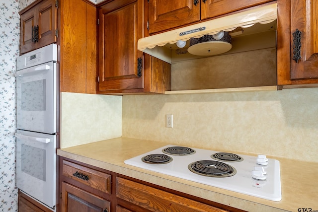 kitchen featuring light countertops, white appliances, brown cabinets, and under cabinet range hood