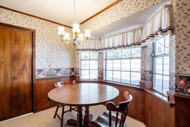 dining space with wallpapered walls, a wainscoted wall, ornamental molding, an inviting chandelier, and a textured ceiling