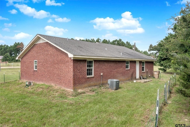 rear view of property featuring central air condition unit and a yard