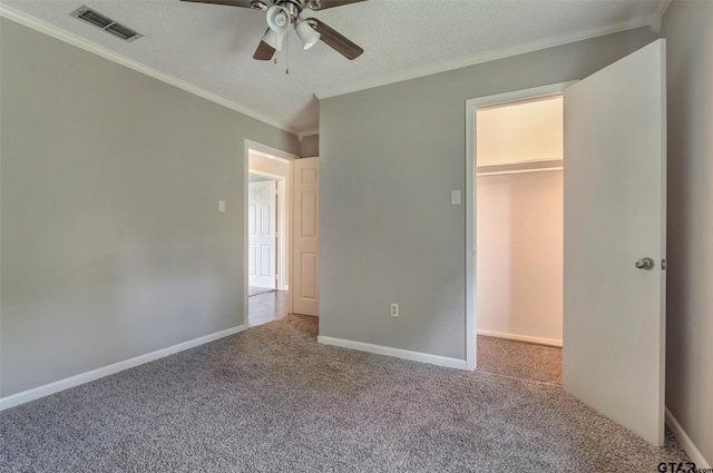 unfurnished bedroom featuring carpet, ceiling fan, crown molding, a spacious closet, and a closet