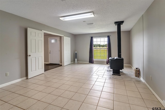 unfurnished room with a wood stove, light tile patterned floors, and a textured ceiling