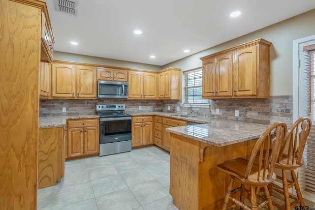 kitchen with a breakfast bar area, visible vents, a peninsula, a sink, and stainless steel appliances