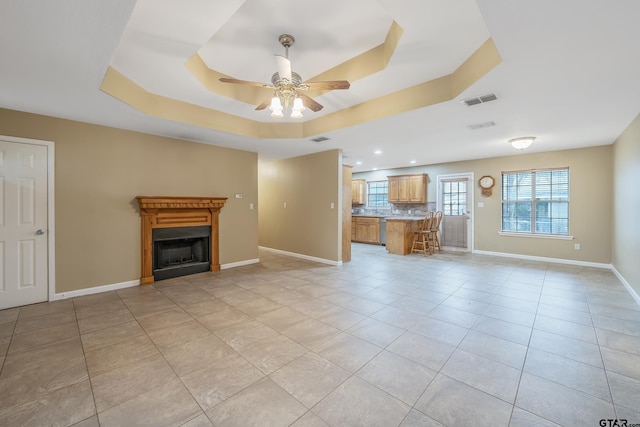 unfurnished living room with a tray ceiling, a ceiling fan, visible vents, and baseboards