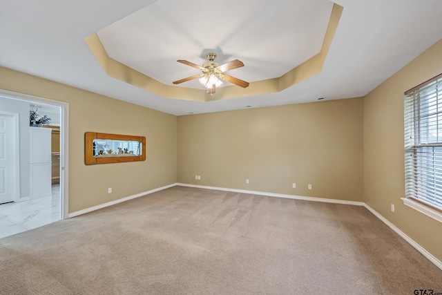 unfurnished room with light colored carpet, a ceiling fan, a raised ceiling, and baseboards