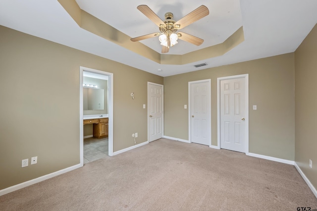 unfurnished bedroom featuring baseboards, visible vents, a tray ceiling, ensuite bathroom, and light colored carpet