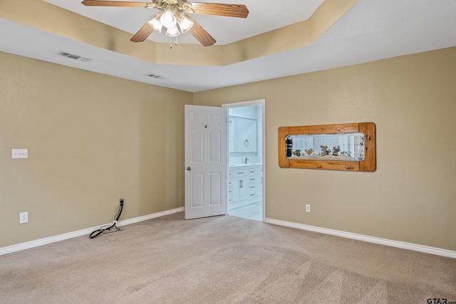 empty room featuring a raised ceiling, carpet flooring, baseboards, and visible vents