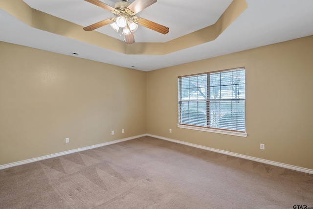 carpeted empty room featuring a tray ceiling, baseboards, and ceiling fan