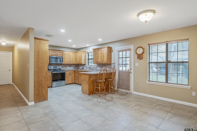 kitchen featuring visible vents, a peninsula, stainless steel appliances, a kitchen bar, and backsplash