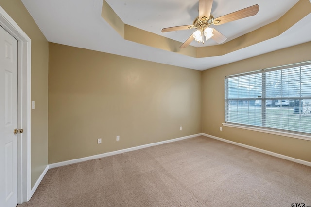 spare room featuring light colored carpet, a raised ceiling, baseboards, and ceiling fan