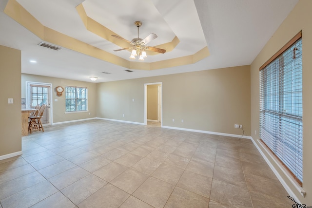 empty room with light tile patterned floors, a tray ceiling, baseboards, and visible vents