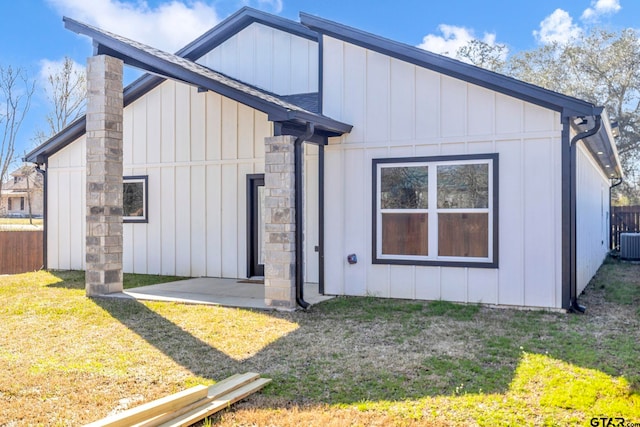 rear view of house with cooling unit, fence, a yard, a shingled roof, and board and batten siding